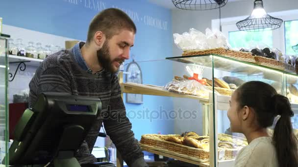 Jonge mannelijke baker werken bij zijn winkel helpen meisje desserts kiezen - Video