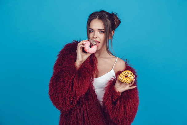Atractiva joven en abrigo de piel brillante posando con rosquillas en las manos
. - Foto, imagen