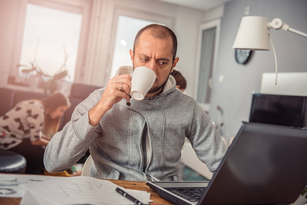 Man drinking coffee and working on laptop at home - Фото, изображение