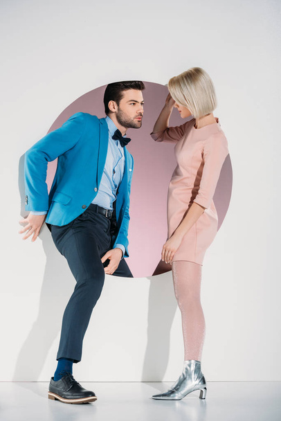 fashionable couple in love looking at each other while stepping through hole on grey   - Photo, Image