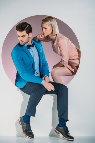 stylish young couple looking away while sitting together in aperture on grey  - Foto, imagen