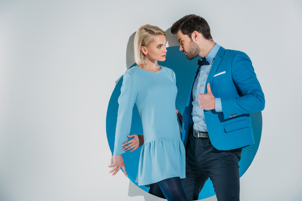 hermosa pareja joven de moda mirándose mientras está de pie en la abertura azul en gris
 - Foto, imagen