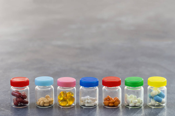 Medicine Concept: line of Medicine Tablets in glass Bottle with multi colored plastic caps on slate background - Foto, afbeelding