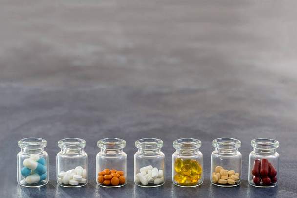 Medicine Concept: line of Medicine Tablets in opened glass Bottle with multi colored plastic caps on slate background - Fotoğraf, Görsel