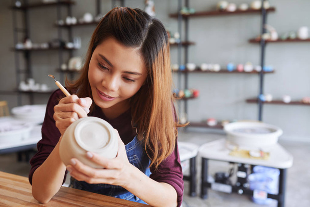 Asian woman creating potter carving surface of clay mug - Zdjęcie, obraz