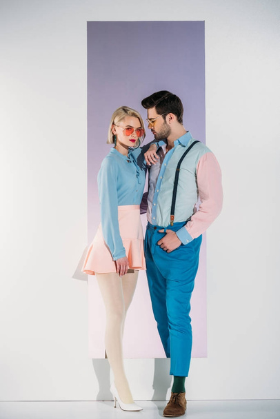 side view of fashionable young couple in sunglasses standing together in opening on grey - Fotoğraf, Görsel