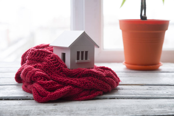 house in winter - heating system concept and cold snowy weather with model of a house wearing a knitted cap - Foto, Imagen