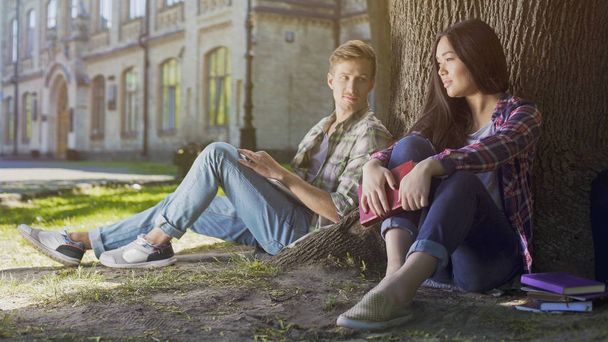 Guy under tree looking at girl sitting next to him, love at first sight feelings - 写真・画像