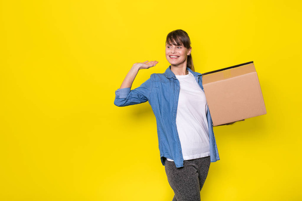 pretty woman standing on yellow background with moving cardboard box - Fotó, kép