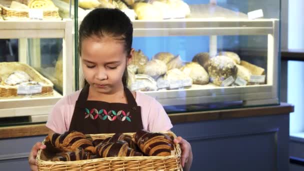 Roztomilá holčička v zástěře pracuje v pekárně drží košík s pečivo - Záběry, video