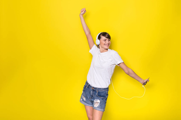 young and beautiful woman listening music with white headphones on isolated on yellow background - 写真・画像