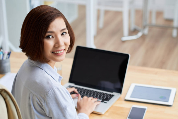 Smiling young business woman working on laptop and looking at camera - Foto, Imagen
