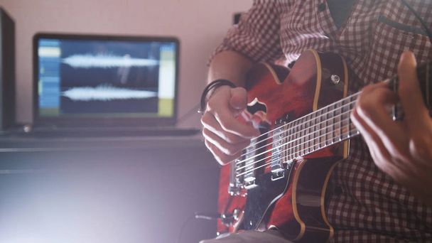 Young male musician composes and records soundtrack playing the guitar using computer - 写真・画像
