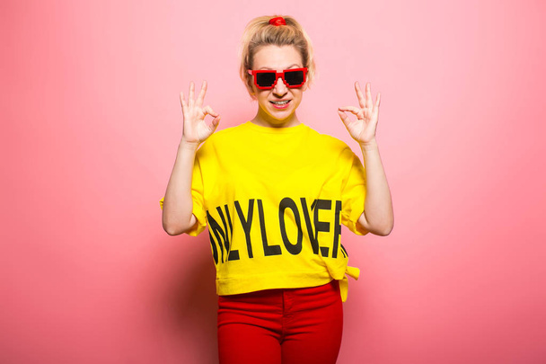 ピンク色の背景に明るい黄色の t シャツとサングラスを着て表現力豊かな女性 - 写真・画像