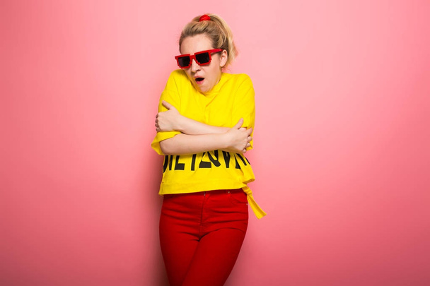 Young expressive woman wearing bright yellow t-shirt and sunglasses on pink background - Foto, Imagem