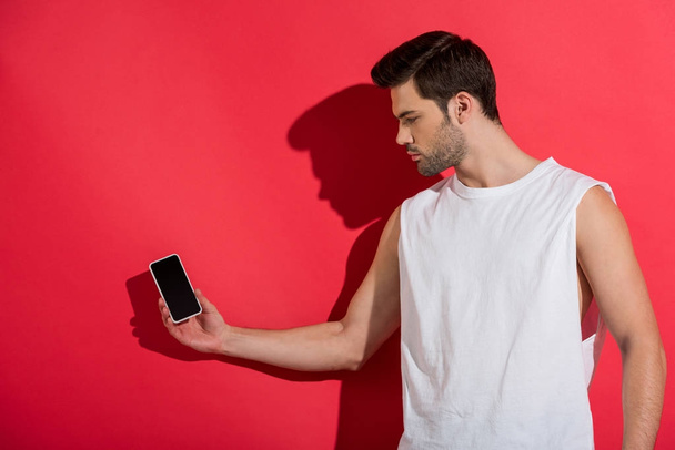 handsome young man holding smartphone with blank screen on pink - Foto, Imagen