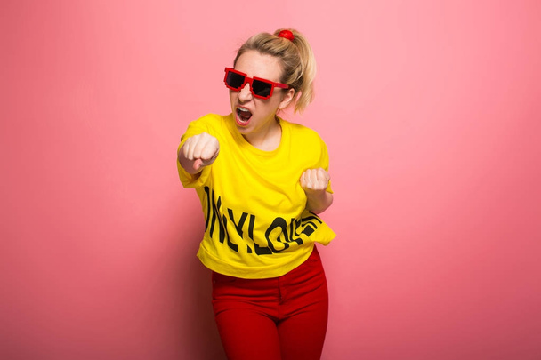 Giovane donna espressiva indossa brillante t-shirt gialla e occhiali da sole su sfondo rosa
 - Foto, immagini
