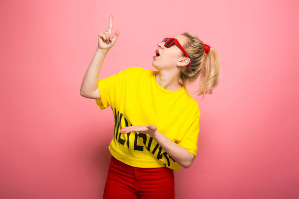 Jeune femme expressive portant un t-shirt jaune vif et des lunettes de soleil sur fond rose
 - Photo, image