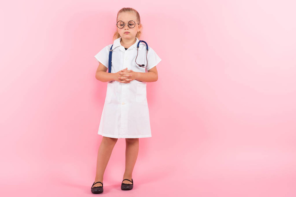 Linda niña en uniforme médico con estetoscopio sobre fondo rosa
 - Foto, imagen