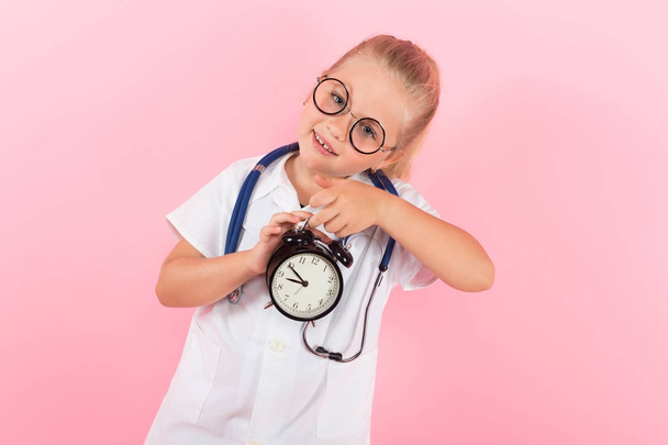 Linda niña en uniforme médico con estetoscopio y reloj sobre fondo rosa
 - Foto, imagen