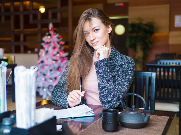 Beautiful successful young business woman enjoying creative job in cafe interior solving project in good mood, smiling entrepreneur checking notes in dairy making schedule of daily work holding pen - Φωτογραφία, εικόνα
