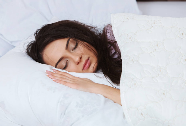 Kız evde beyaz bir yatakta uyuyor. Yatakta evde, üstten görünüm beyaz keten üzerinde pijama içinde uyuyan genç kadın. - Fotoğraf, Görsel