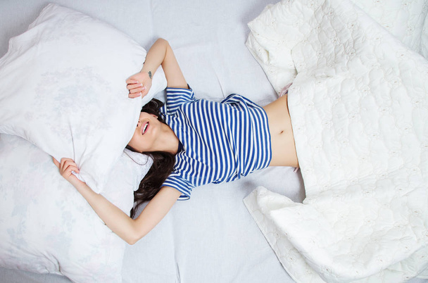 Mädchen schläft zu Hause in einem weißen Bett. junge Frau schläft in Nachtwäsche auf der weißen Bettwäsche im heimischen Bett, Draufsicht. - Foto, Bild