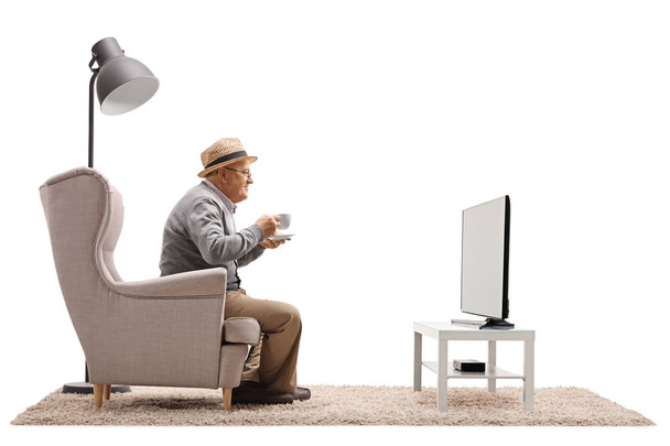 man with a cup sitting in an armchair and watching television  - Фото, изображение