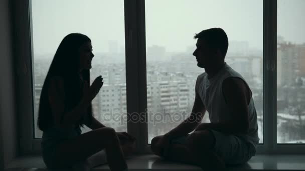 Joven pareja feliz sentada en el alféizar de la ventana, hablando emocionalmente, discutiendo y gesticulando
 - Metraje, vídeo