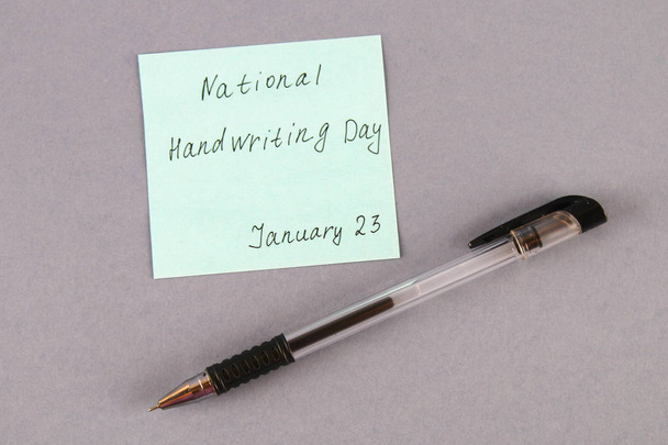 A note with an inscription is a national day of hand writing and a pen on a gray background. - Photo, Image
