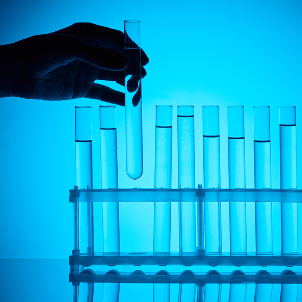 imagen recortada de farmacia femenina tomando tubo de vidrio con sustancia de pie sobre azul
 - Foto, Imagen