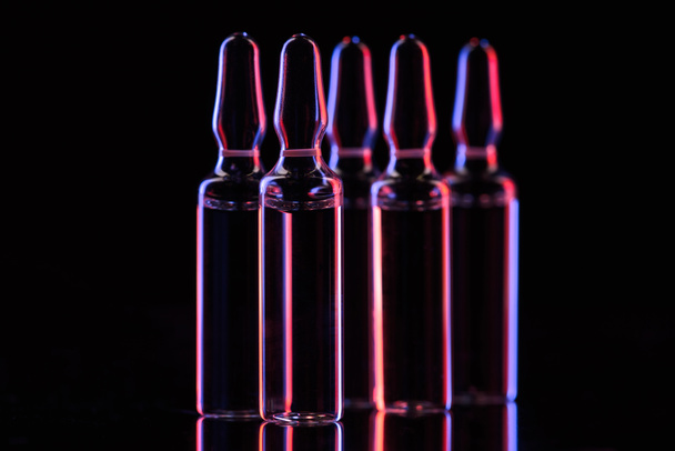 transparent glass ampoules with liquid and reflection on table on black - Φωτογραφία, εικόνα