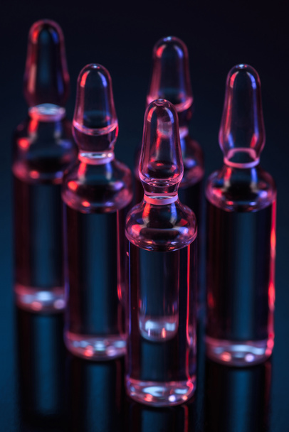 primer plano de cinco ampollas de vidrio transparente con líquido sobre la mesa sobre negro
 - Foto, Imagen