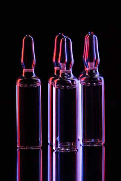 ampollas de vidrio transparente con reflejo de luz en la mesa sobre negro
 - Foto, imagen