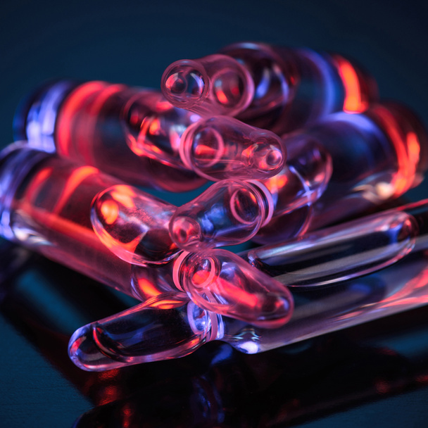 close up of transparent glass ampoules with red light reflection on table - Photo, Image
