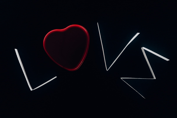 Wortliebe aus Papierstreifen und rotem Herz isoliert auf schwarzem Valentinstag-Konzept - Foto, Bild
