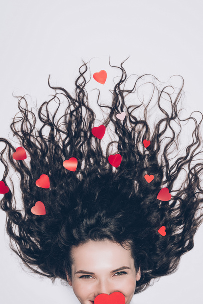 happy young woman with little red hearts in her curly hair isolated on white - Фото, изображение