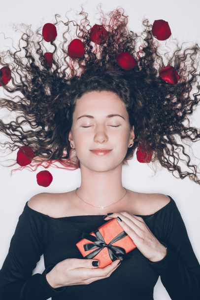 attraente giovane donna con i capelli ricci in possesso di regalo isolato su bianco
 - Foto, immagini