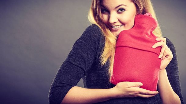 Woman hugs hot water bottle in red fleece cover - Foto, afbeelding