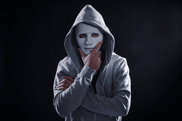 Masked hacker wearing hoodie in darkness - Foto, Imagen