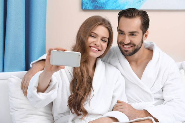 Young loving couple in bathrobes taking selfie at home - Фото, изображение