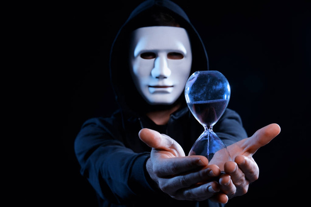 Masked hacker with sand clock in darkness - Zdjęcie, obraz