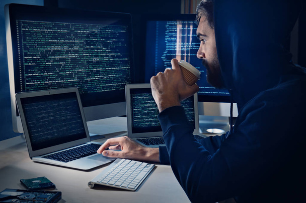 Man drinking coffee while hacking server in dark room - Фото, изображение