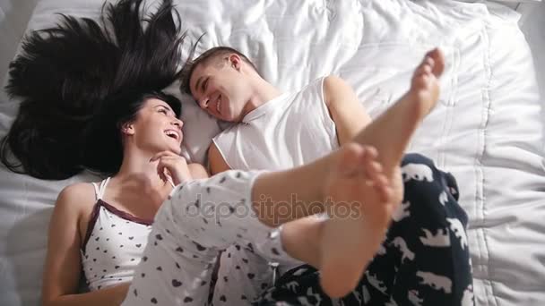 ベッド、笑みを浮かべて、お互いに、持ち上げ、足に触れて幸せな愛情のあるカップルを上から表示します。 - 映像、動画