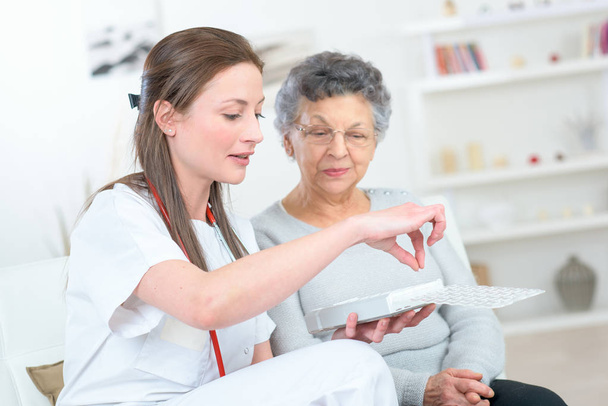 Νοσοκόμα συζητώντας φαρμακευτική αγωγή με ηλικιωμένη γυναίκα - Φωτογραφία, εικόνα