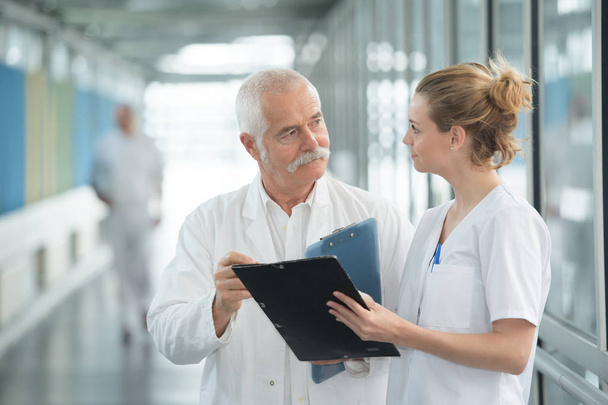 Personal médico con portapapeles hablando en el pasillo del hospital
 - Foto, Imagen