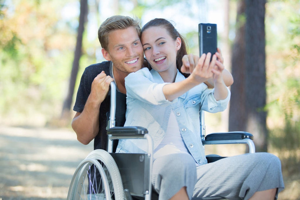 woman in wheelchair and boyfriend taking a selfie with smartphone - Zdjęcie, obraz