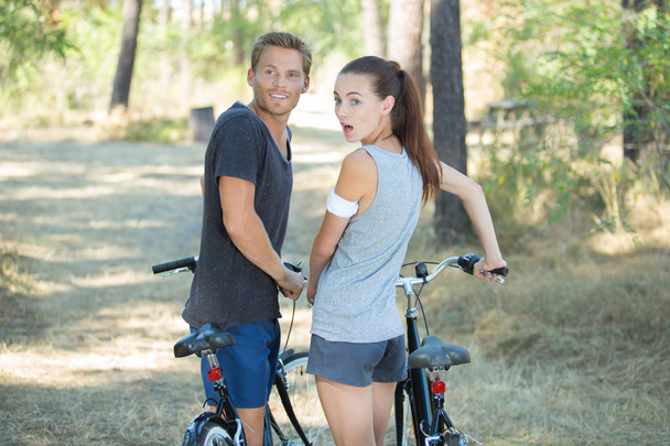 young surprised couple with bicycles in forest - Zdjęcie, obraz