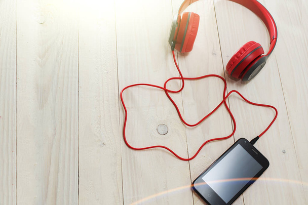 red headphones and phone on wooden light background. - Valokuva, kuva