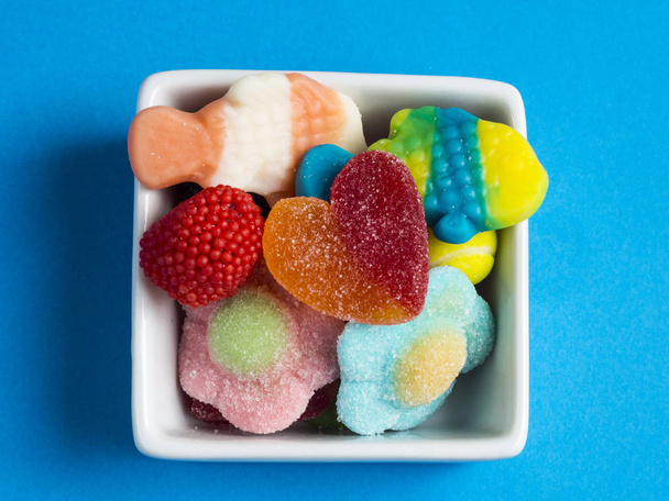 Caramelos de gelatina en un bol sobre fondo azul
 - Foto, Imagen